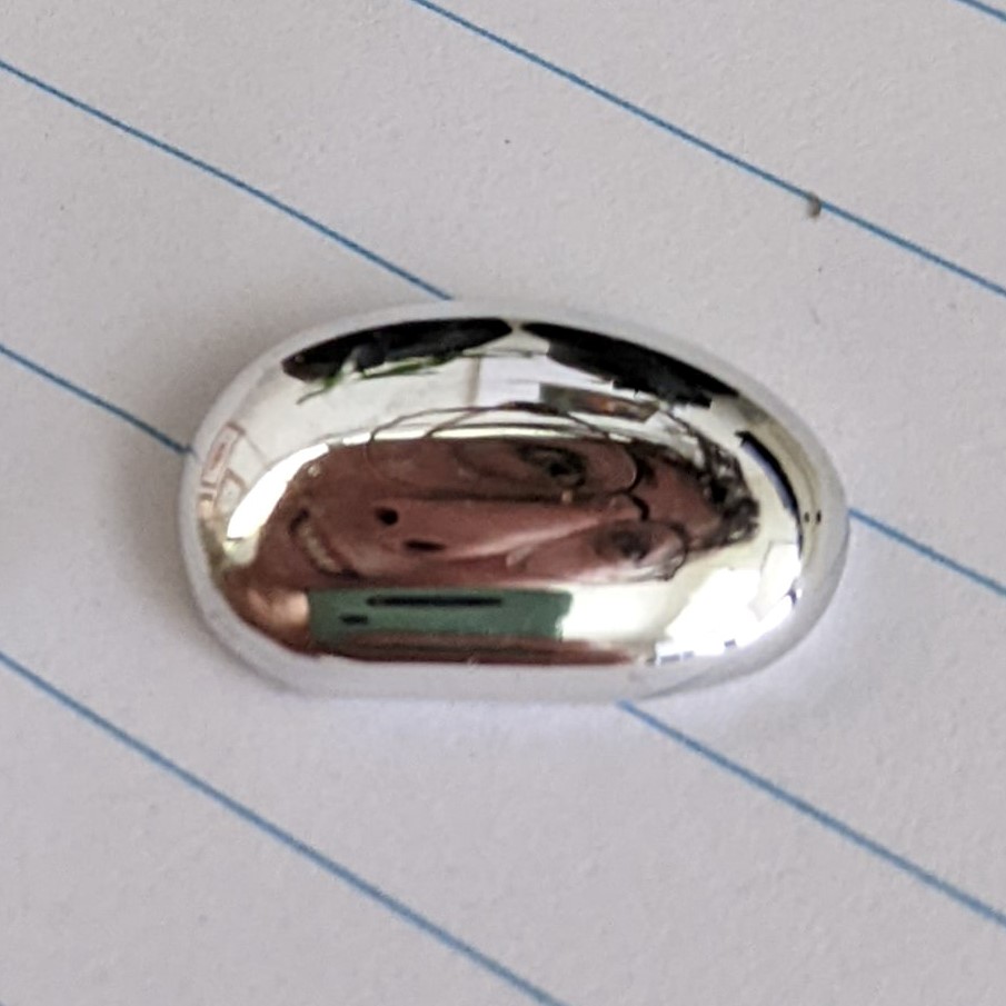 A selfie taken using the reflective surface of a silver blob of gallium. The shape of the blob means the face is really distorted. 